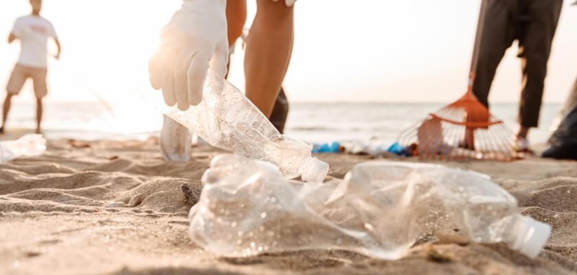 Pludmalē tiek vākti atkritumi, plastmasas pudeles. 