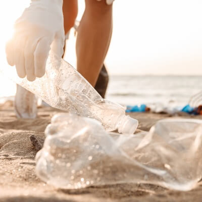 Pludmalē tiek vākti atkritumi, plastmasas pudeles.