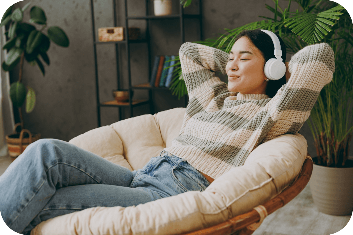 Женщина сидит в удобном кресле и слушает наушники Bluetooth.