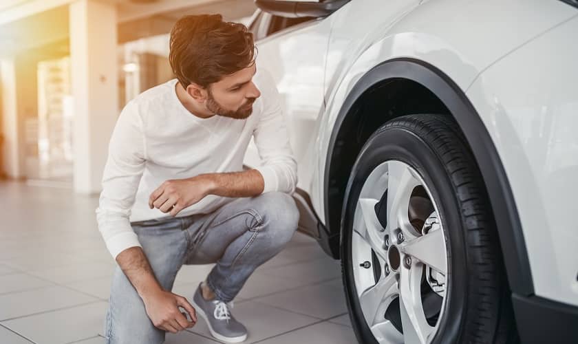 Перед покупкой подержанного автомобиля мужчина проверяет шины.