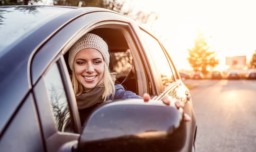 Sieviete skatās auto spogulī, lai izvairītos no auto bojājumiem.